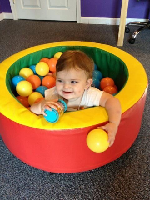 A happy toddler playing in a colorful ball pit at the clinic