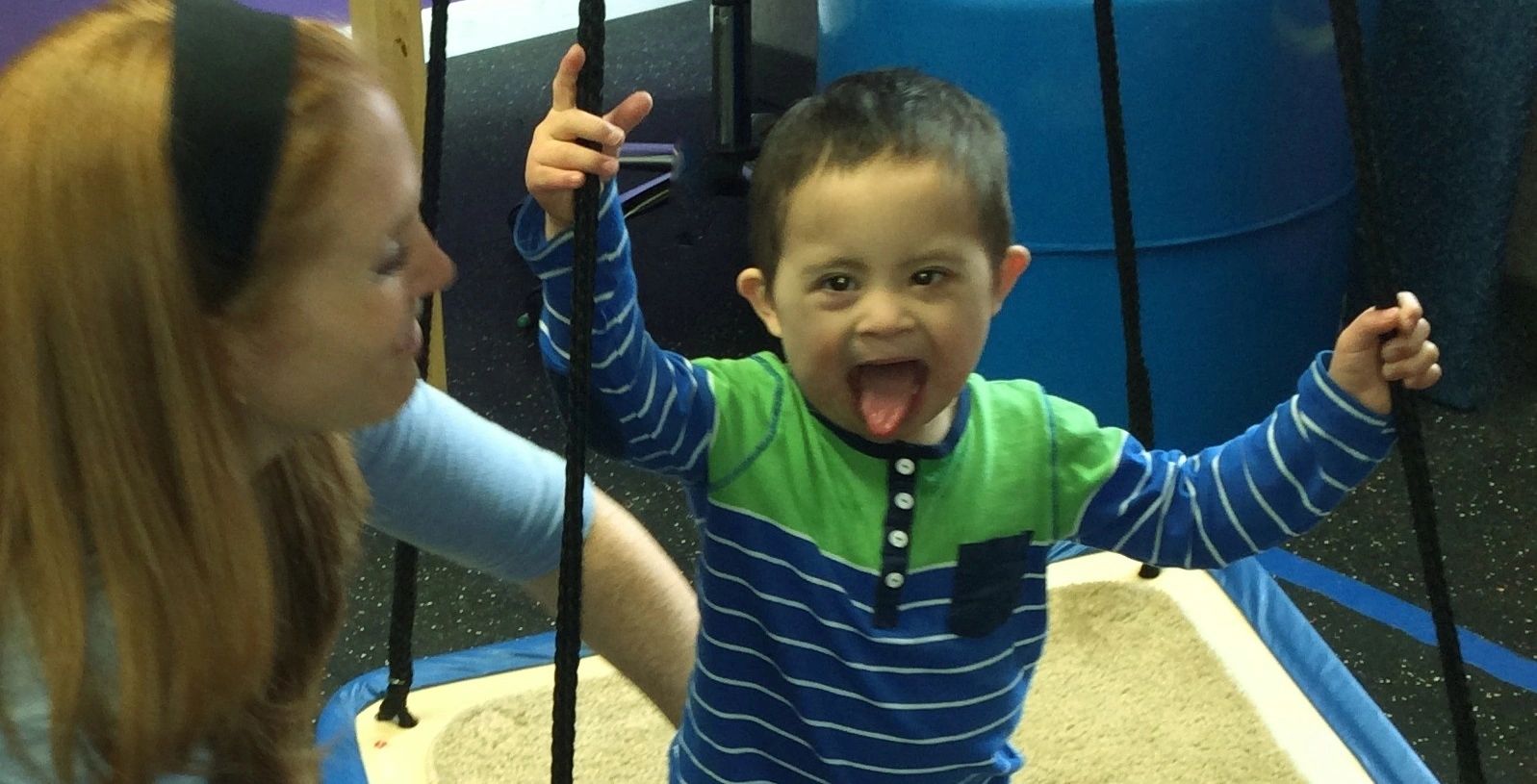 A smiling boy holding the ropes of a platform swing during a therapy session